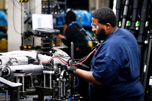 Работник прикачва кабелен сноп към шасито на модел X S.U.V. в завод на BMW в Гриър, Южна Каролина