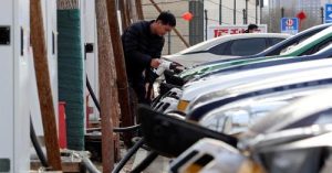 Мъж държи щепсел за зареждане на автомобил в станция за зареждане на електрически превозни средства (EV) Smart Charge в Пекин, Китай