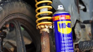 Бутилка WD-40 до ръждясал амортисьор с жълта пружина, мръсна джанта и гума до него
