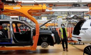 Монтажният работник на Stellantis се разхожда между два автомобила Jeep Grand Cherokee L 2021 г. на монтажната линия в комплекса за сглобяване в Детройт - завода Mack в Детройт, Мичиган, САЩ.